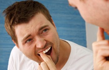 A concerened man looking at a mirror and checking his teeth
