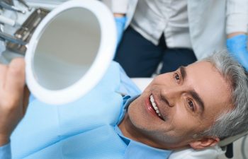 A happy mature man sitting in a dental chair after a treatment and looking and his nteeth and gums in a mirror